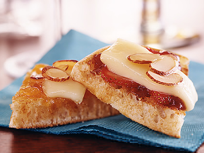 A wedge of a bays english muffin topped with cheese, fruit and almonds
